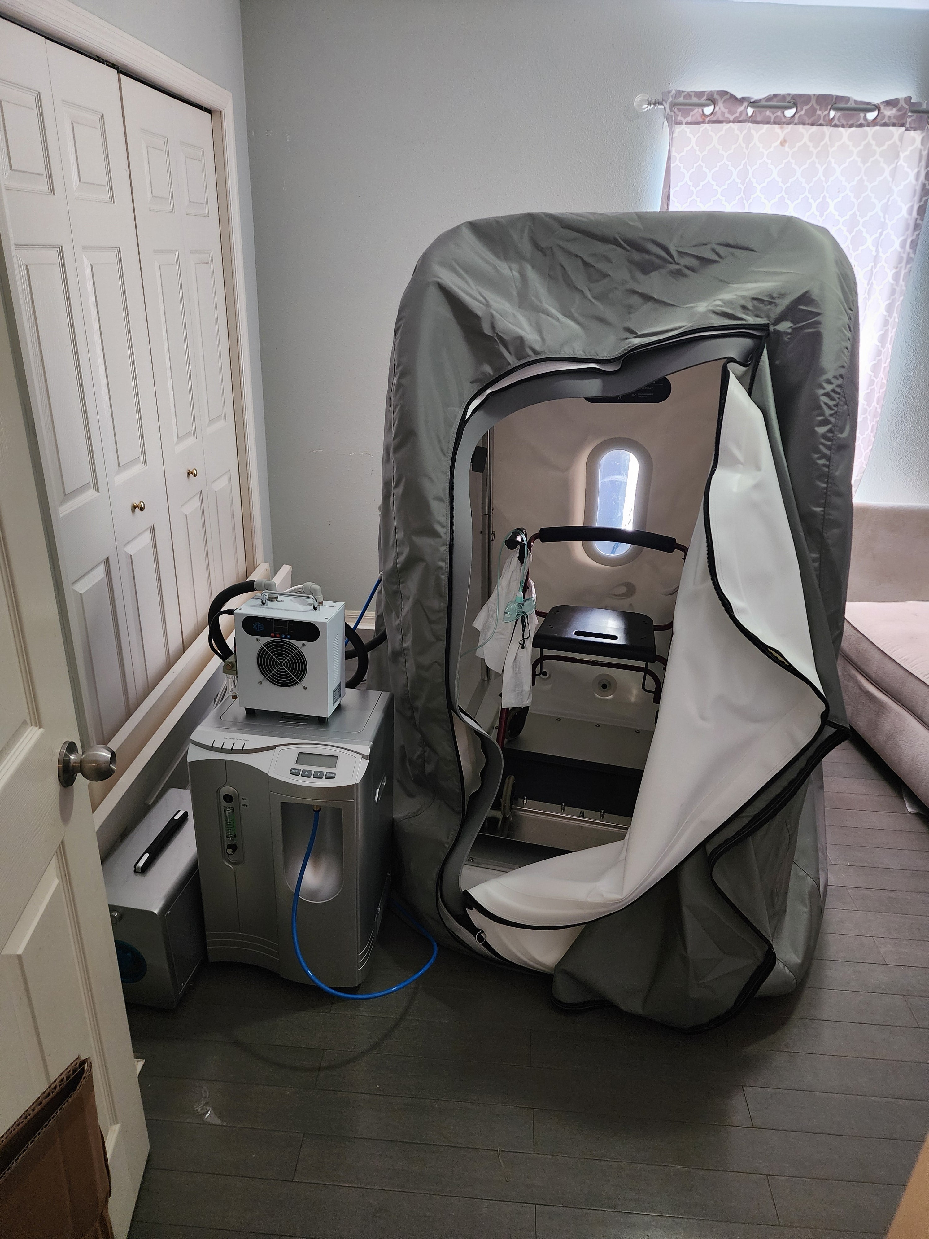 Sitting hyperbaric chamber in a gray room on a wooden floor with accessory units attached