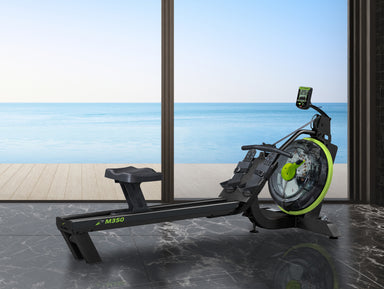 Rowing machine with M360 branding in a room with large windows showing a beach view.