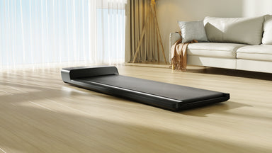 Black electronic walking pad on a wooden floor with a modern living room in the background