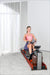 Woman exercising on a rowing machine in a bright room with large windows.