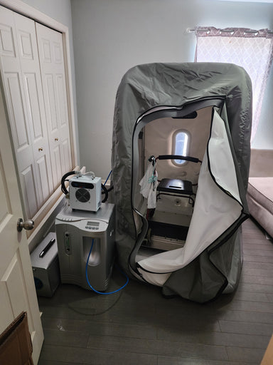 Sitting hyperbaric chamber in a gray room on a wooden floor with accessory units attached