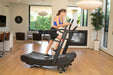 Woman exercising on a treadmill in a home setting with a fireplace and plants.