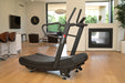 Treadmill in a modern living room with large windows and a fireplace.