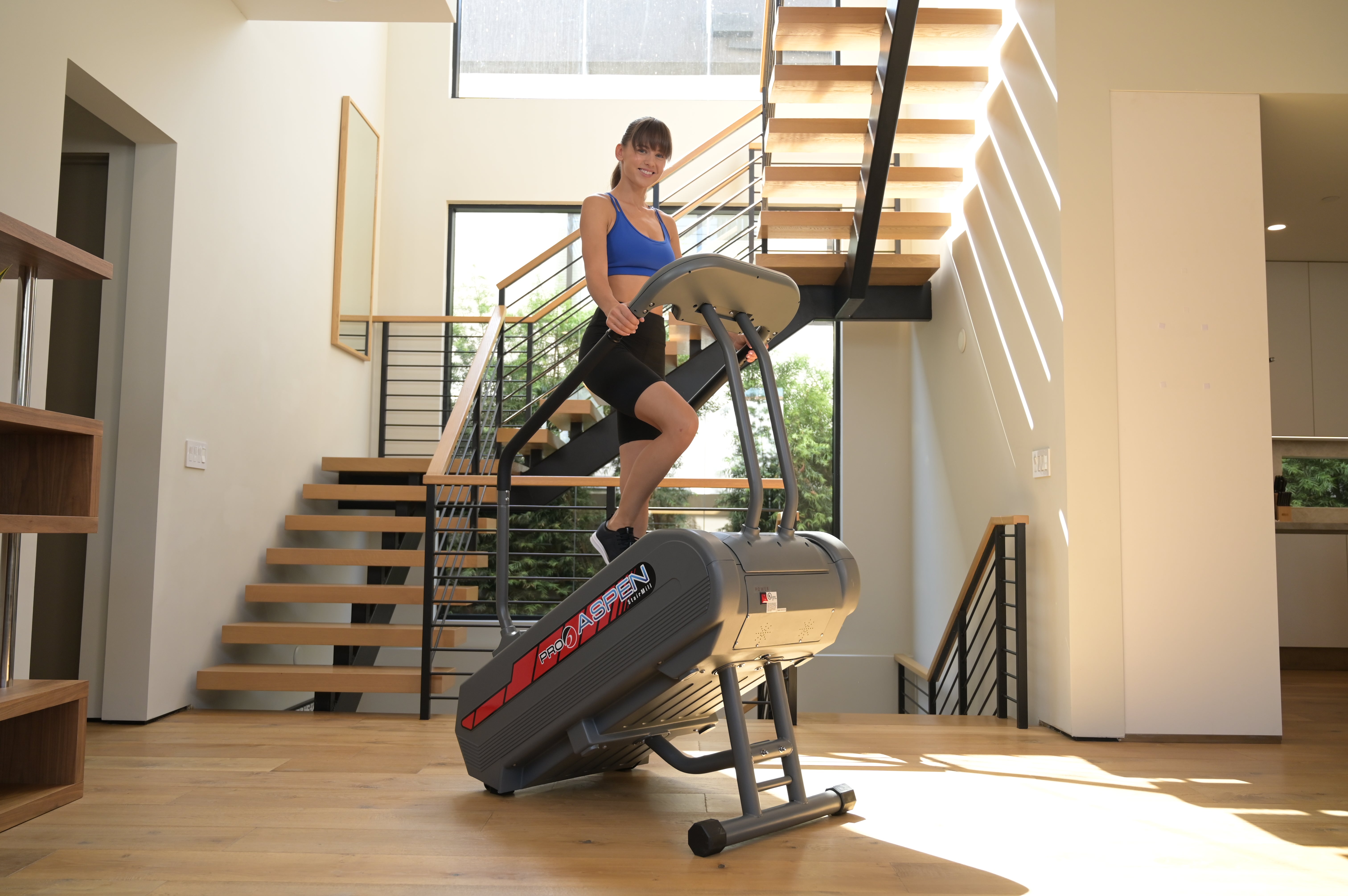 Woman using a stair stepper machine in a home setting with a staircase in the background