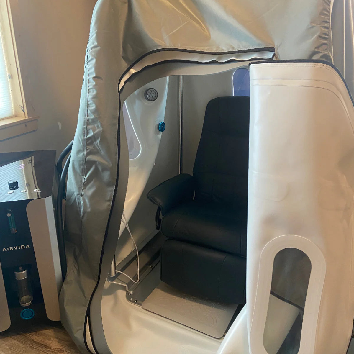 Personal airlock with a black seat inside, next to an air purifier labeled 'AIRVIDA'.