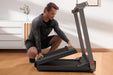 Man folding a treadmill in a room with wooden flooring and white walls.