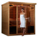 Woman standing in a wooden infrared sauna with a white towel wrapped around her.
