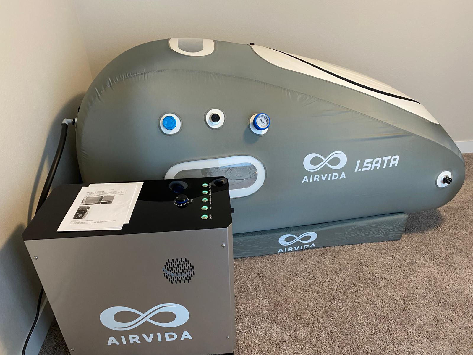 Hyperbaric chamber with AIRVIDA branding on a carpeted floor against a wall.