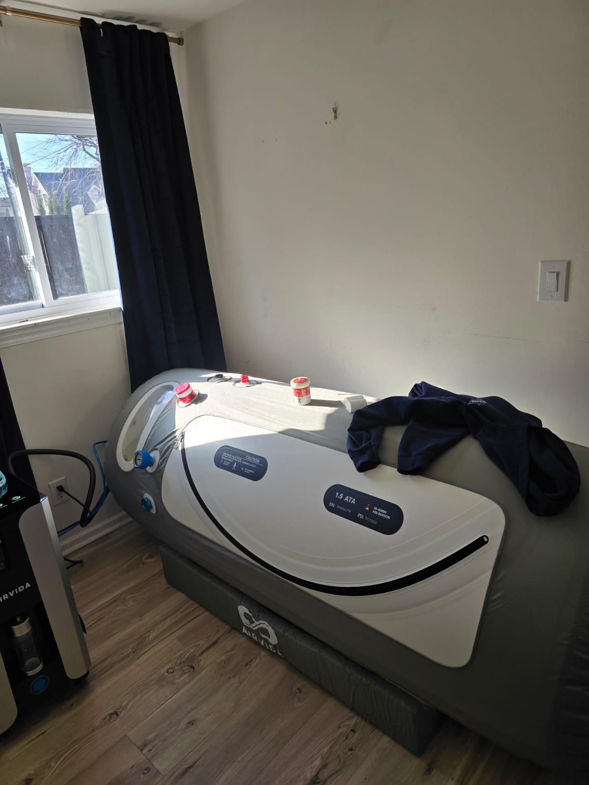 Gray and white hyperbaric chamber in front of a window in a white room on a wooden floor