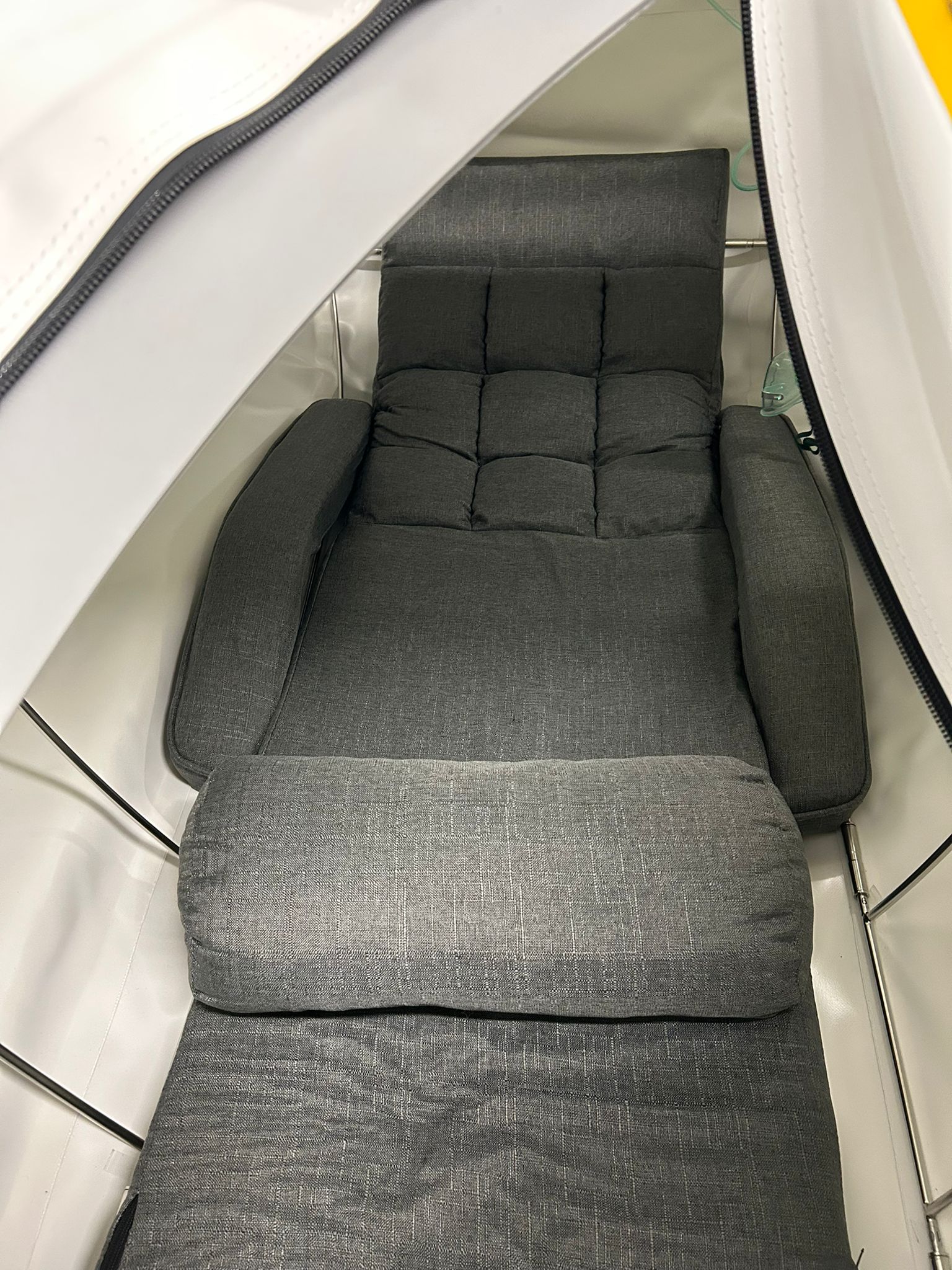 Gray cushioned chair inside a hyperbaric chamber with a white interior.