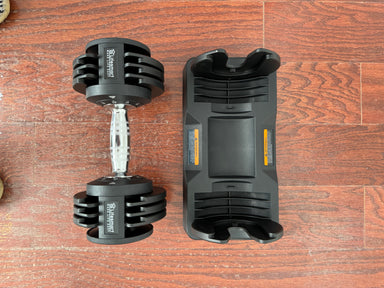 Black adjustable dumbbell and its packaging on a wooden surface