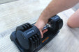 Person using a adjustable dumbbell on a carpeted floor