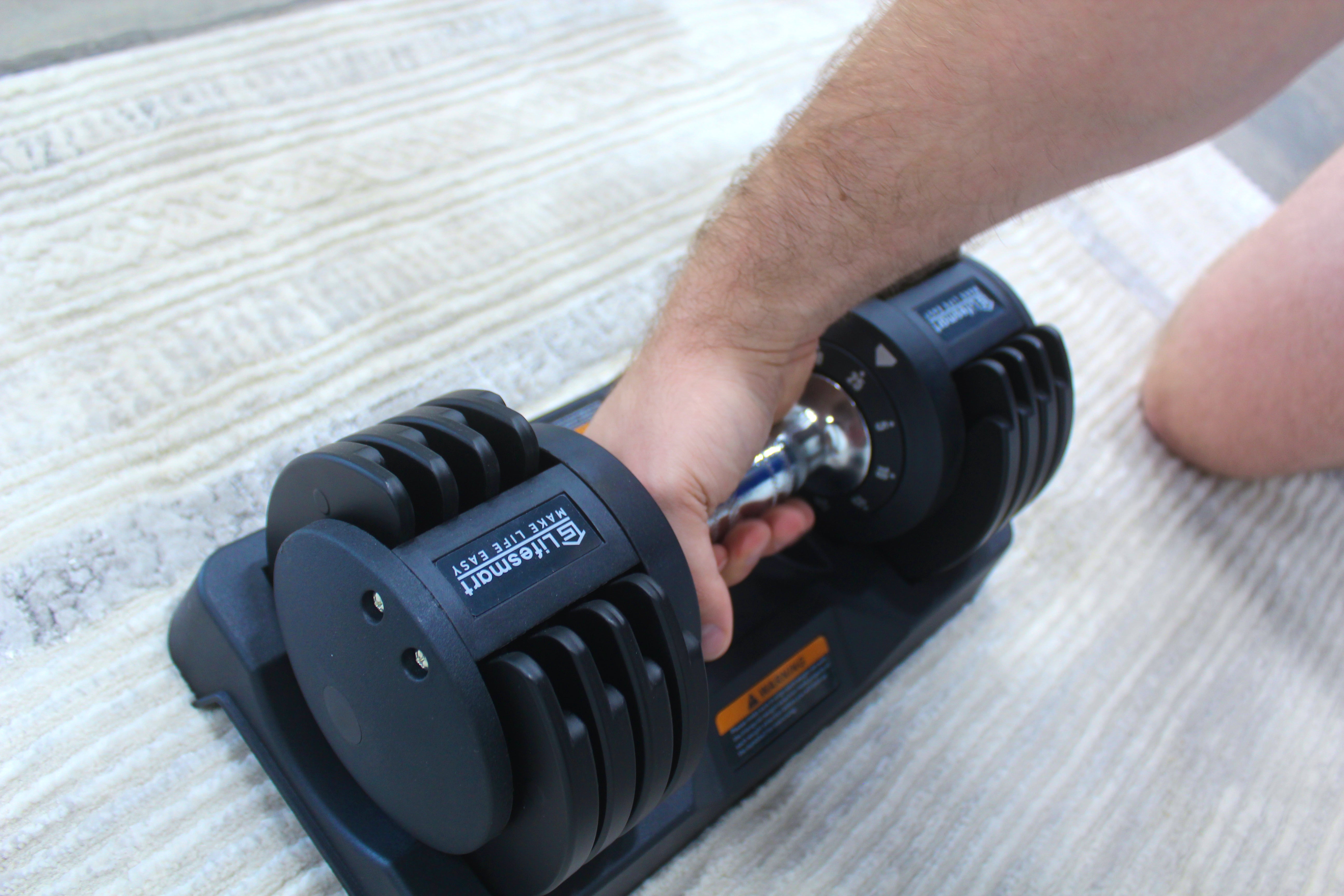 Person using a adjustable dumbbell on a carpeted floor