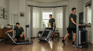 Three men using treadmills in a home setting with large windows and curtains.