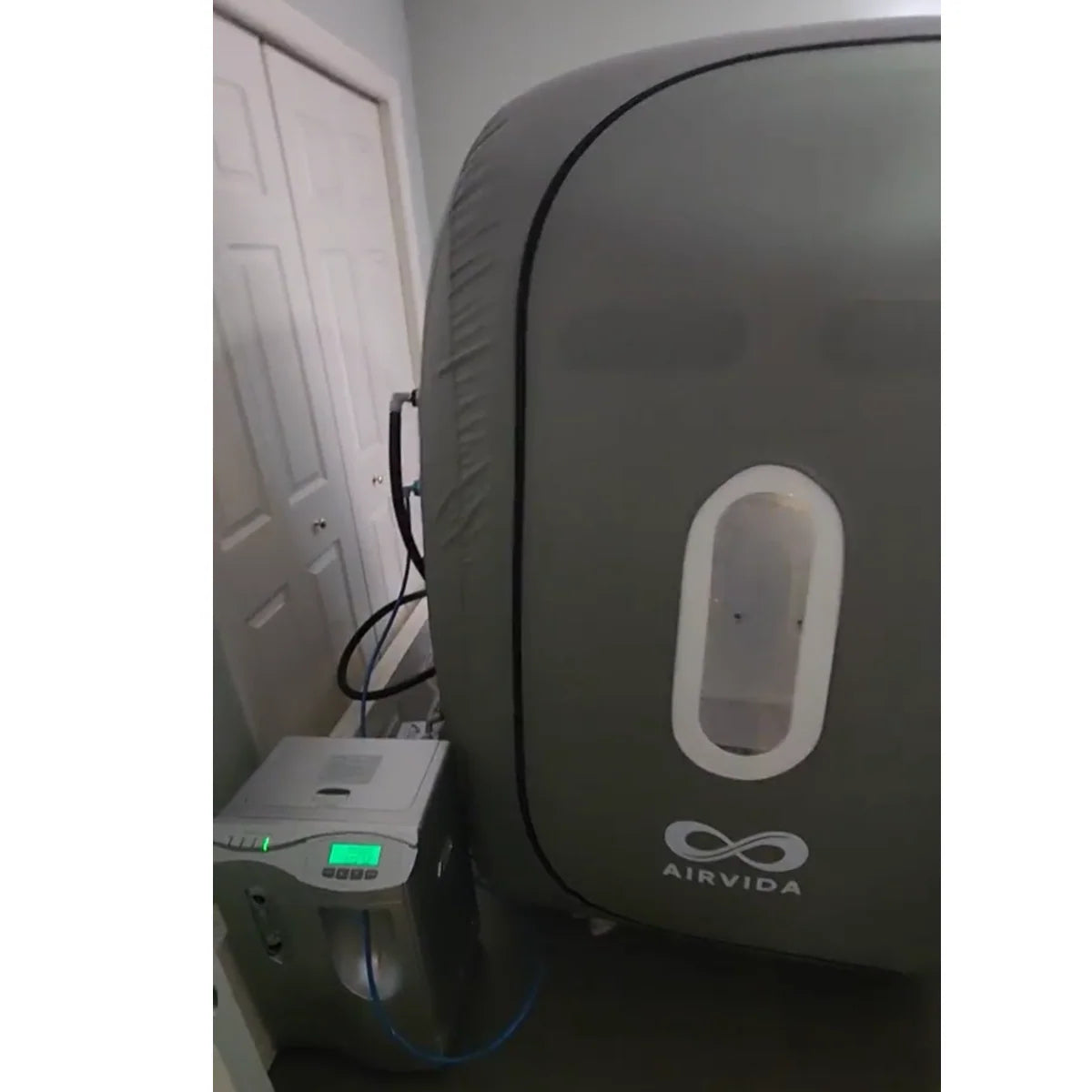 Sitting hyperbaric chamber in a gray room on a wooden floor with accessory units attached